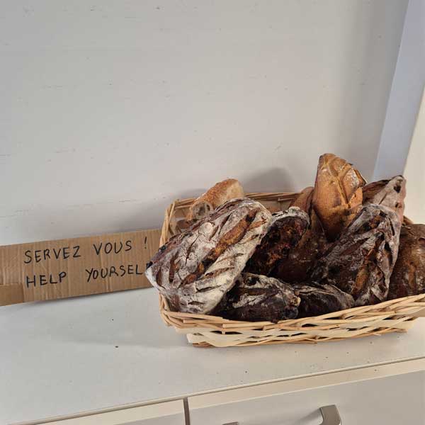 Un panier avec différentes sortes de pain avec un carton sur lequel est écrit : Servez-vous !